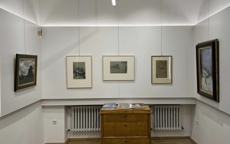 Galerieansicht mit mehreren gerahmten Bildern und einem Holzsideboard.
